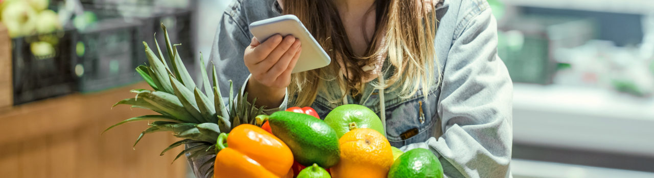 A picture of a woman buying groceries while using a mobile phone.
